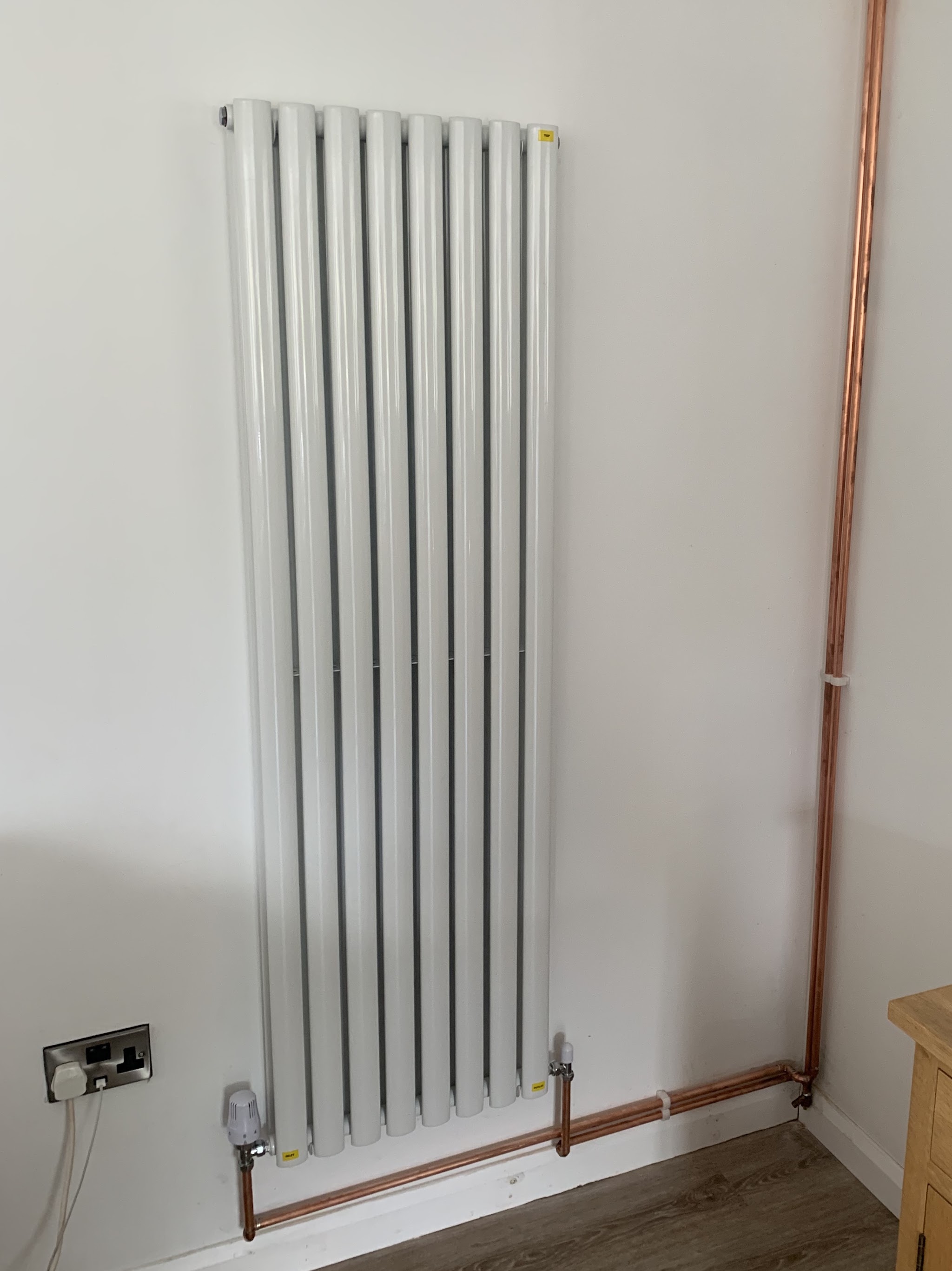 A tall white vertical designer radiator fitted with a neat copper pipe run