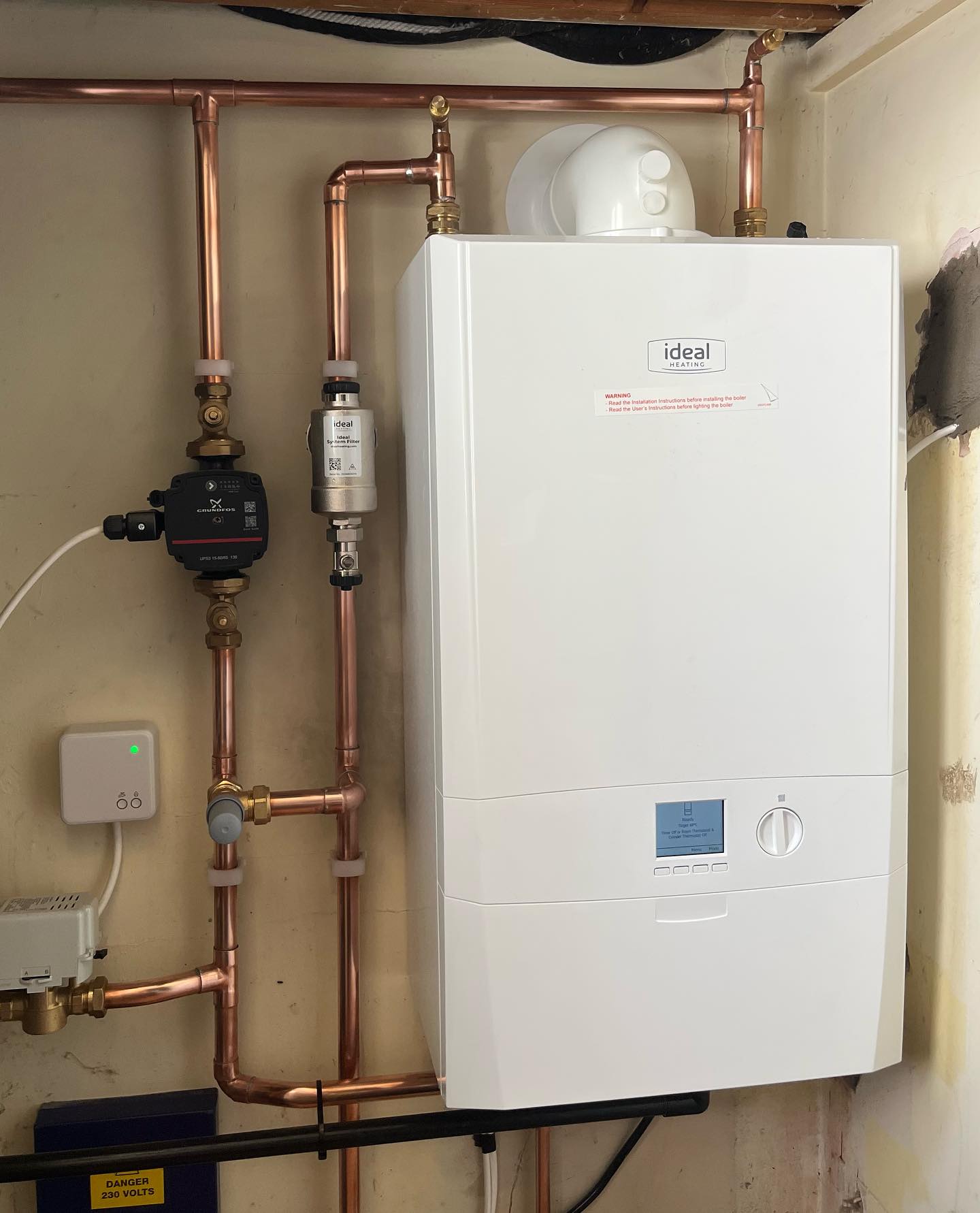 A new Ideal boiler on the wall with neat copper pipework, pump and filter below it