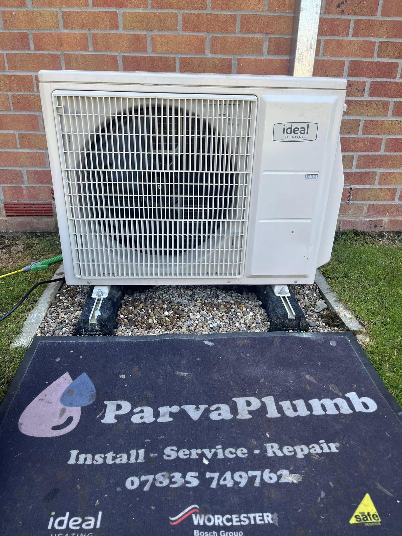 An Ideal air source heat pump on a gravel base, with the ParvaPlumb door mat reading Install, Service, Repair in front of it