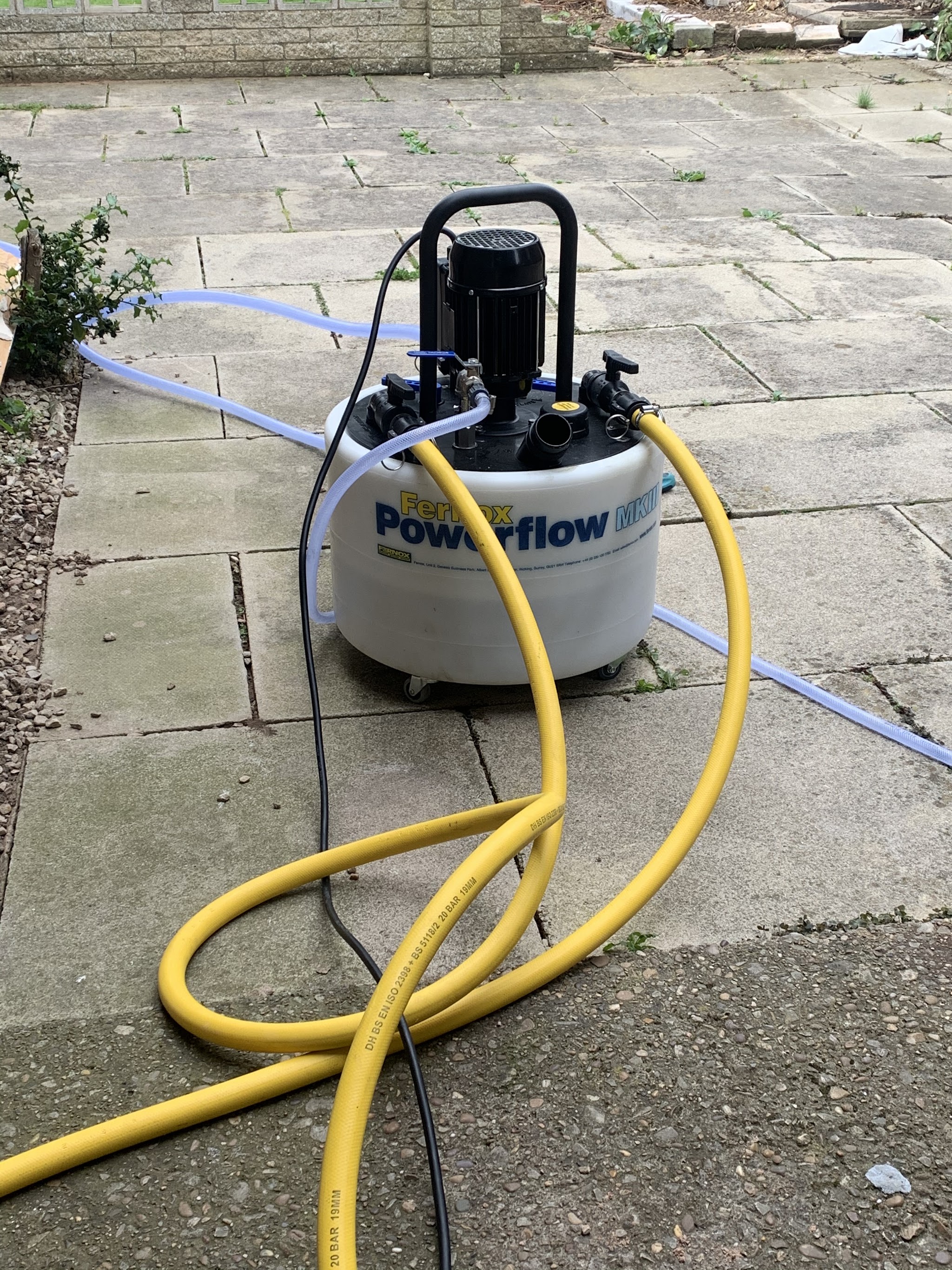 A power flushing machine with yellow hoses set up on a patio