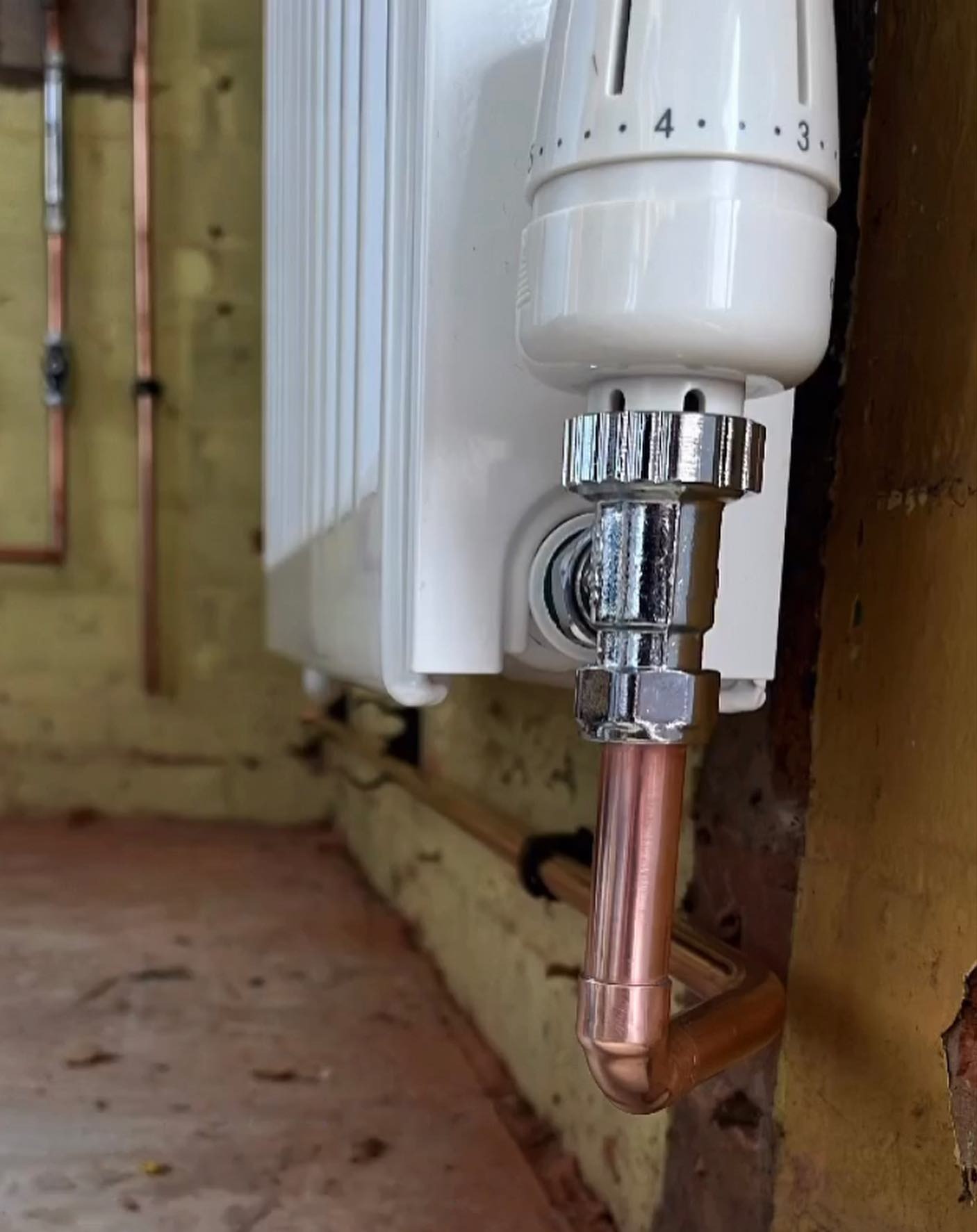 Close-up of a new thermostatic radiator valve and copper tail on a white radiator