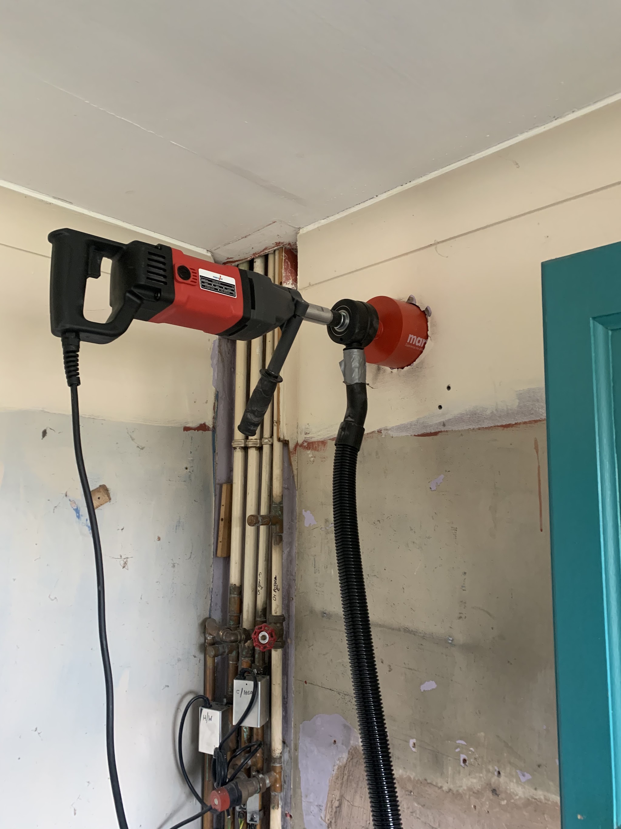 A core drill fixed to a wall, cutting a hole for pipework